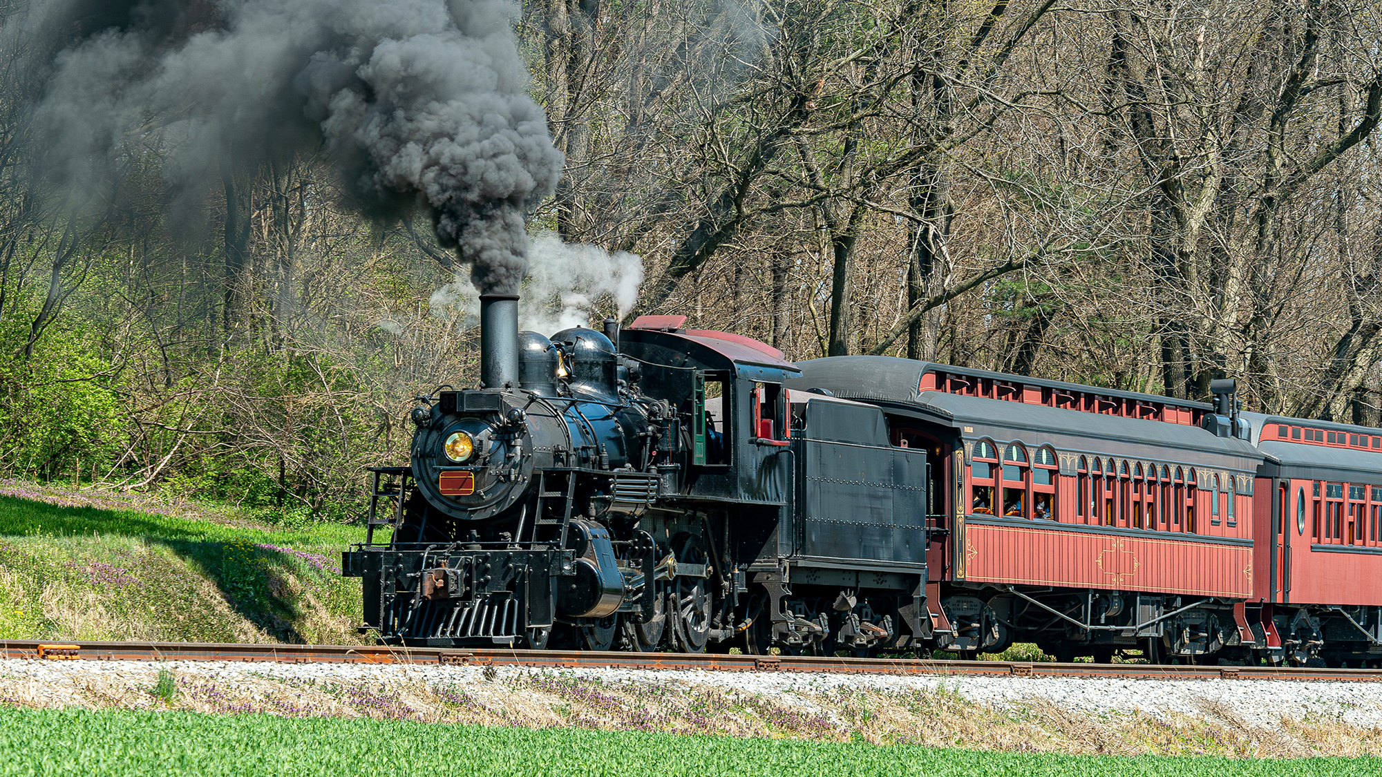 A steam passenger train moving slowly blowing lots of black smoke