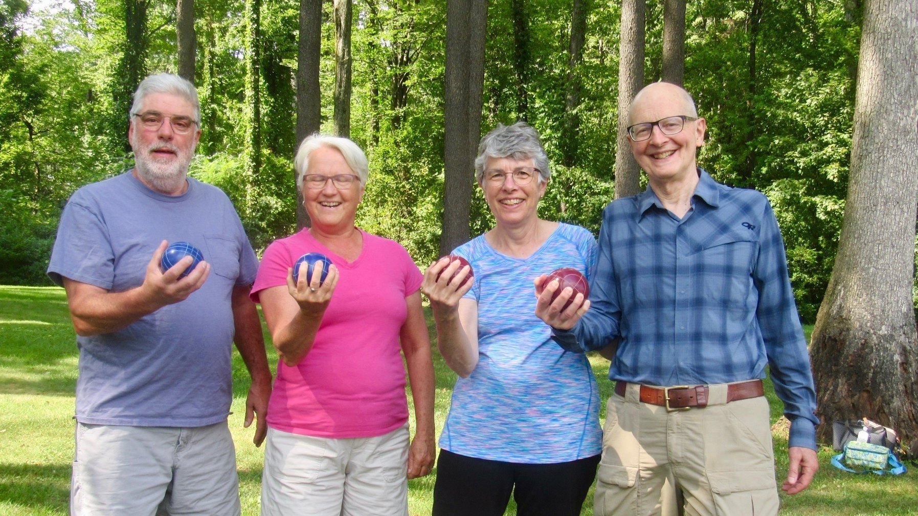 4 people standing outside in a row holding bocce balls.