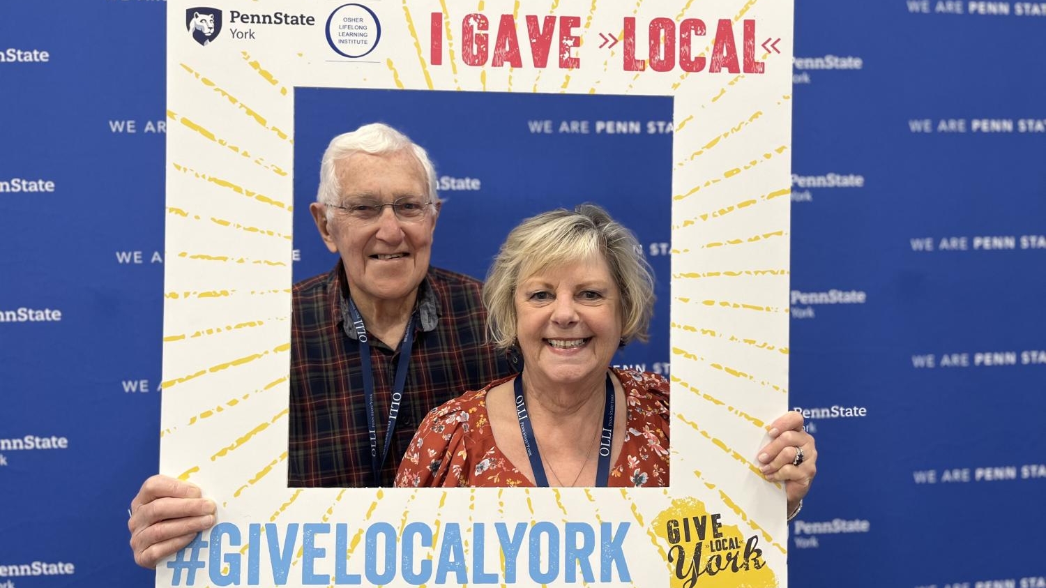 Couple standing with a Give Local York selfie frame