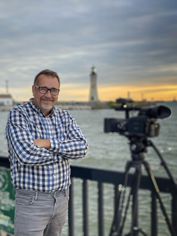 Man standing outside with a lighthouse in the background.