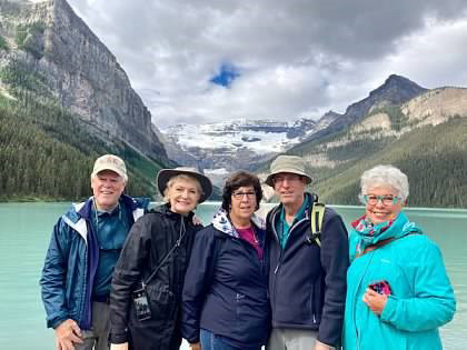 Group of five mature adults standing in front of a body of water and mountains