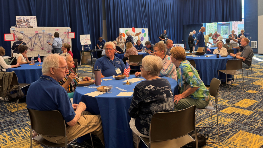 OLLI members sitting at round tables in a large conference room.