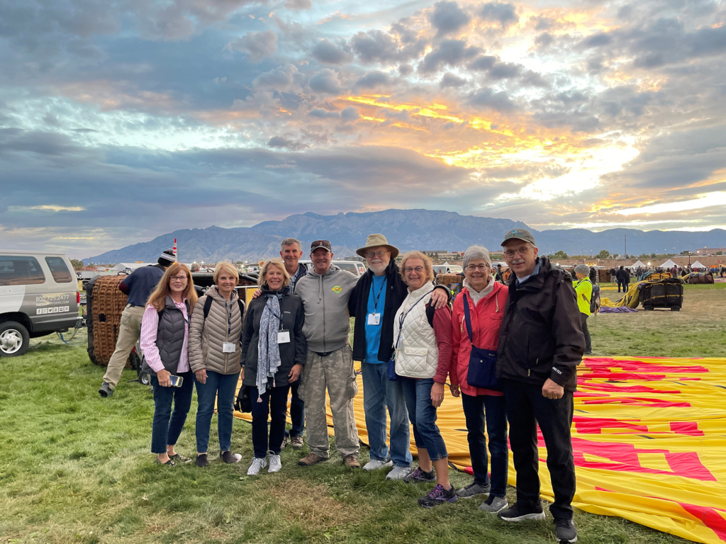 A group of OLLI tour participants pose in front of a deflated hot air balloon with a stunning expanse of sky behind them
