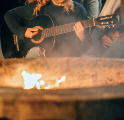 Person playing guitar in front of a fire.