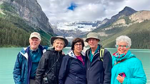 Group of five mature adults standing in front of a body of water and mountains